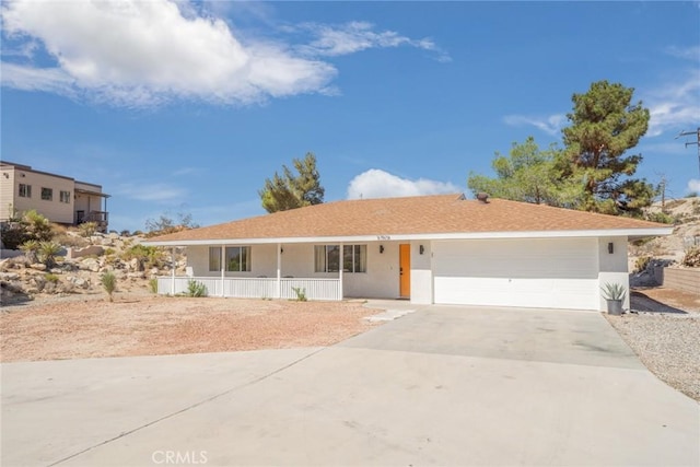 ranch-style home with a porch, concrete driveway, an attached garage, and stucco siding