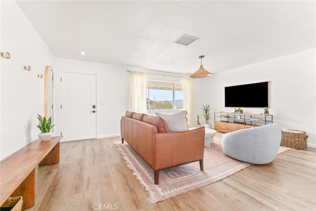 living room featuring visible vents, light wood-style flooring, and baseboards