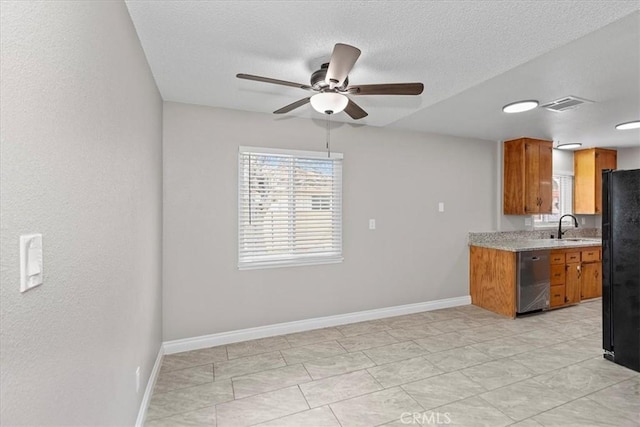 kitchen with brown cabinetry, dishwasher, light countertops, and freestanding refrigerator