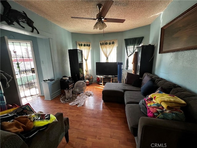 living area with ceiling fan, a textured ceiling, wood finished floors, and a textured wall