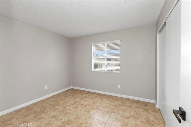 unfurnished bedroom featuring a closet, light tile patterned floors, a textured ceiling, and baseboards