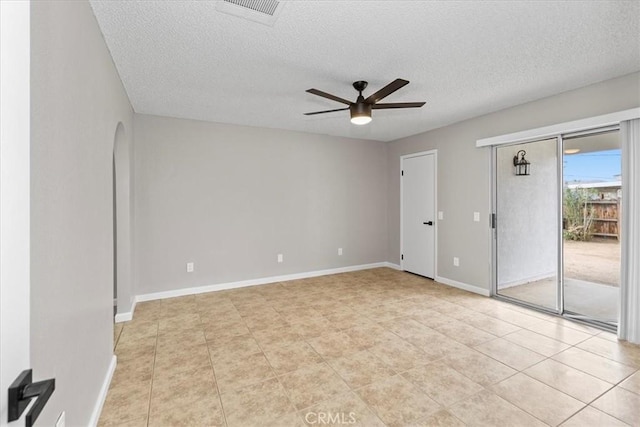 spare room featuring visible vents, a textured ceiling, arched walkways, baseboards, and ceiling fan