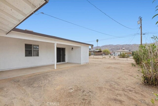 rear view of property with stucco siding, a mountain view, and a patio