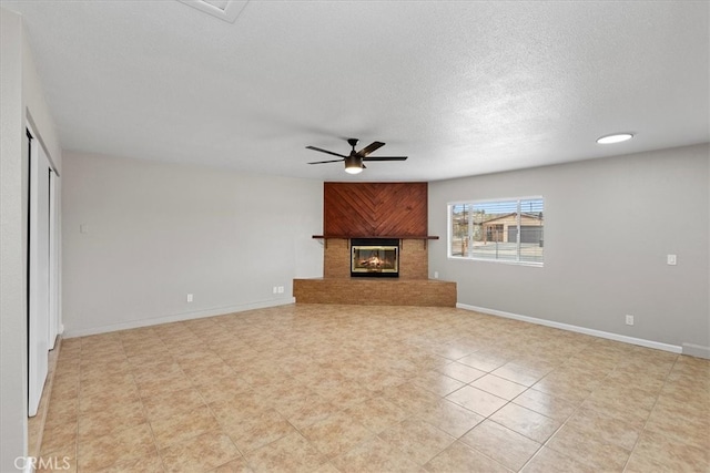 unfurnished living room featuring a glass covered fireplace, a textured ceiling, baseboards, and a ceiling fan