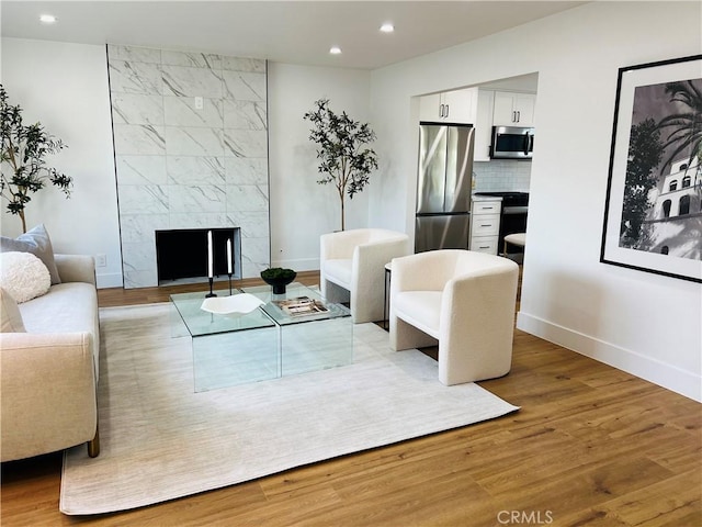 living area with recessed lighting, a premium fireplace, baseboards, and wood finished floors