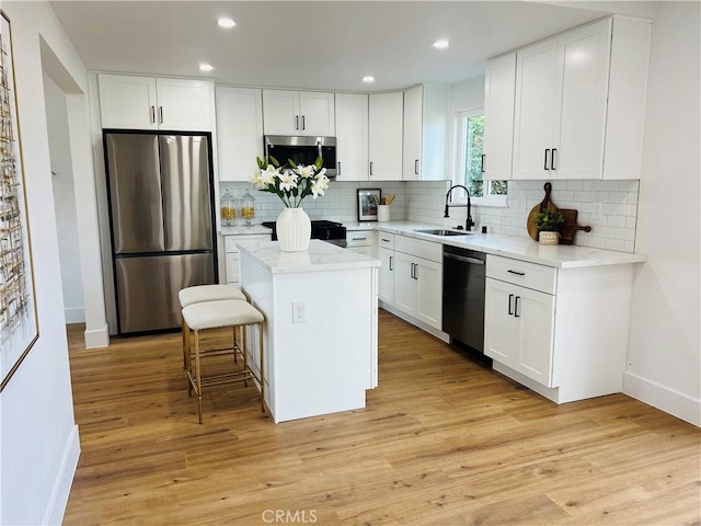 kitchen with light wood finished floors, a kitchen island, a sink, appliances with stainless steel finishes, and white cabinetry