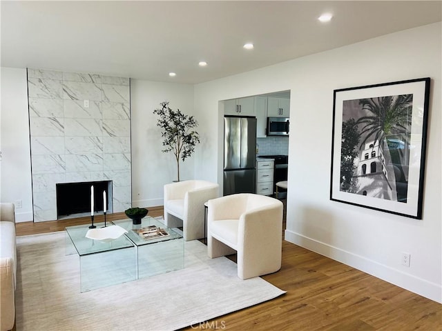 living room featuring a premium fireplace, recessed lighting, baseboards, and wood finished floors