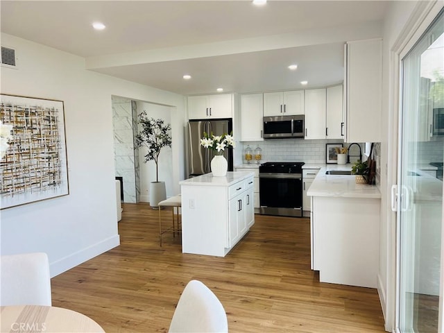 kitchen featuring light wood finished floors, backsplash, appliances with stainless steel finishes, and a sink