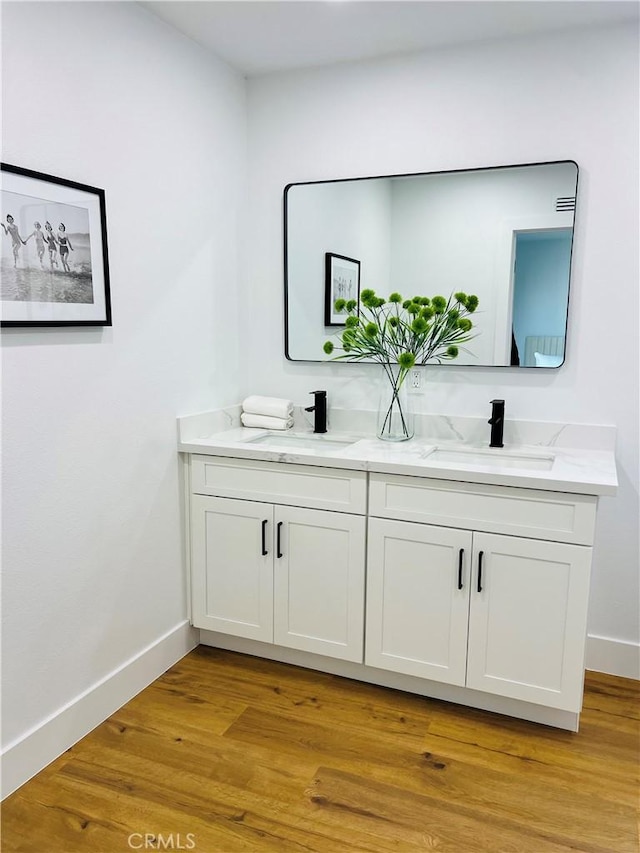 bathroom featuring double vanity, wood finished floors, baseboards, and a sink