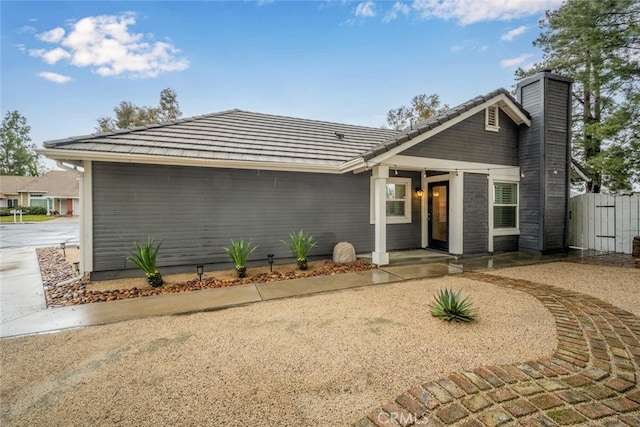 mid-century inspired home featuring a tile roof, fence, and a chimney