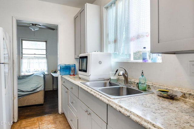 kitchen with freestanding refrigerator, light countertops, a sink, and a ceiling fan