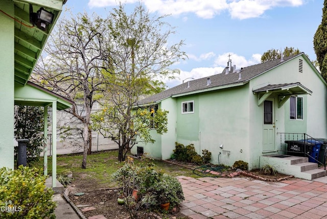 exterior space featuring stucco siding, fence, a patio, and roof with shingles