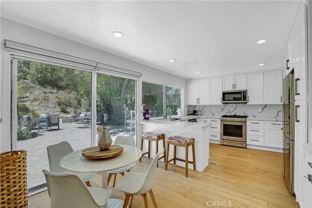 kitchen with light wood finished floors, a kitchen breakfast bar, appliances with stainless steel finishes, a peninsula, and white cabinetry