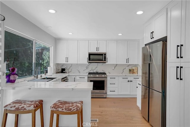 kitchen featuring a peninsula, a sink, stainless steel appliances, white cabinets, and a kitchen breakfast bar