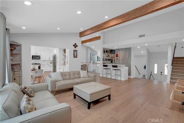 living area with lofted ceiling with beams, recessed lighting, light wood finished floors, indoor bar, and stairs