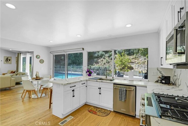 kitchen featuring visible vents, light wood finished floors, a peninsula, a sink, and stainless steel appliances