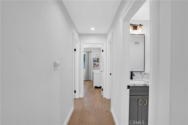 hall featuring a sink, light wood-type flooring, and baseboards