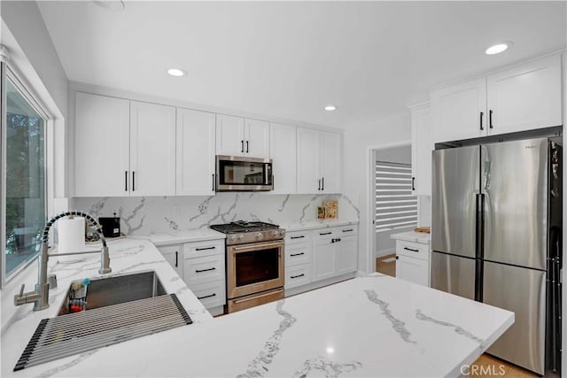 kitchen with tasteful backsplash, appliances with stainless steel finishes, white cabinetry, and a sink