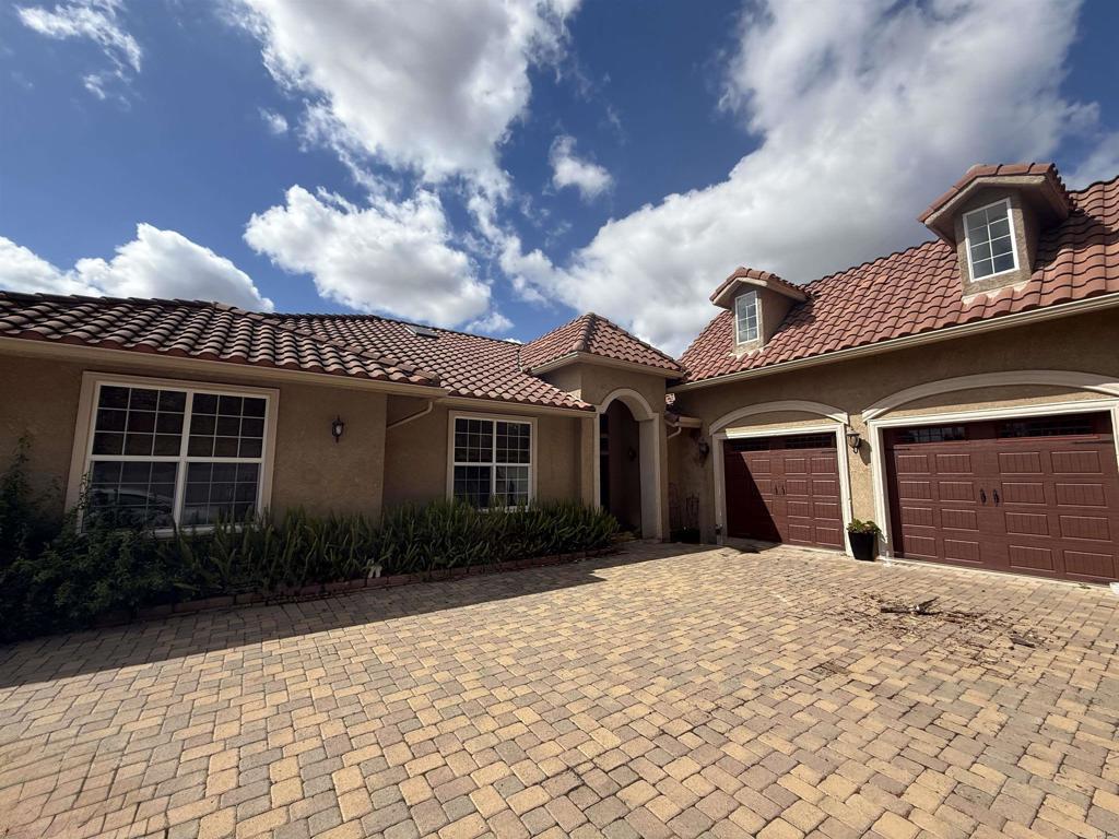 mediterranean / spanish home featuring stucco siding, a tiled roof, decorative driveway, and a garage