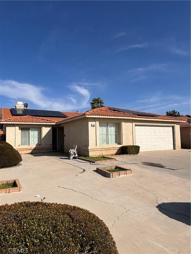 view of front of house with driveway, stucco siding, a garage, a tile roof, and roof mounted solar panels