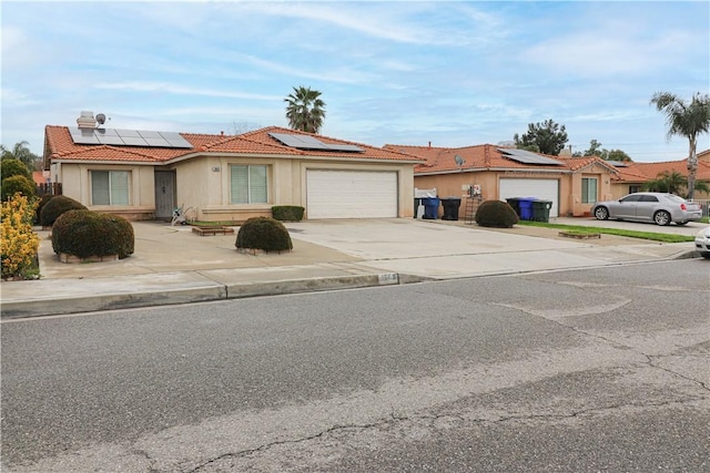 view of front facade featuring solar panels, an attached garage, a tiled roof, stucco siding, and driveway