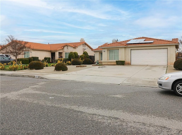 view of front of home featuring solar panels, a tiled roof, stucco siding, a garage, and driveway