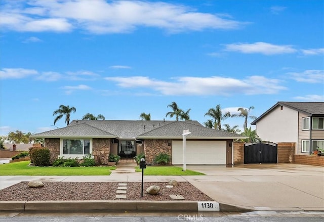 ranch-style home featuring a front lawn, a gate, stone siding, concrete driveway, and a garage