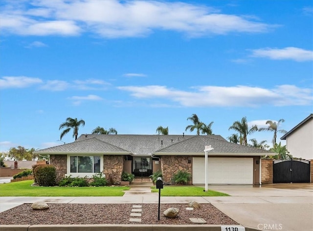 single story home with a front lawn, concrete driveway, stone siding, an attached garage, and a gate