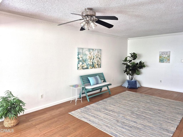 sitting room featuring a ceiling fan, wood finished floors, baseboards, ornamental molding, and a textured ceiling