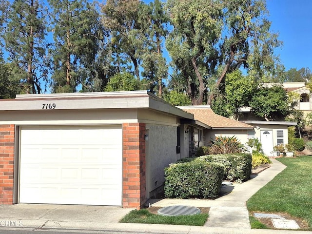 view of front of home with stucco siding, driveway, brick siding, and an attached garage