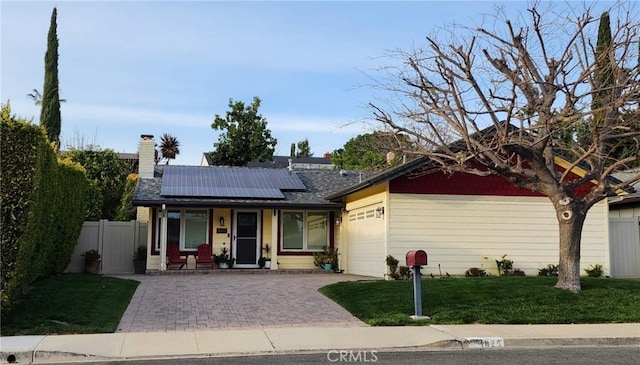 ranch-style home featuring fence, a front yard, roof mounted solar panels, covered porch, and an attached garage