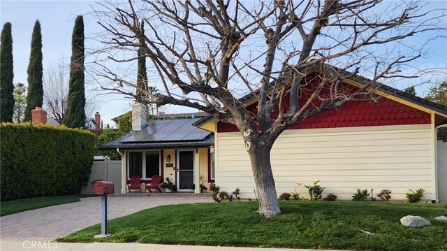 view of front of property with a chimney, solar panels, a front yard, and fence