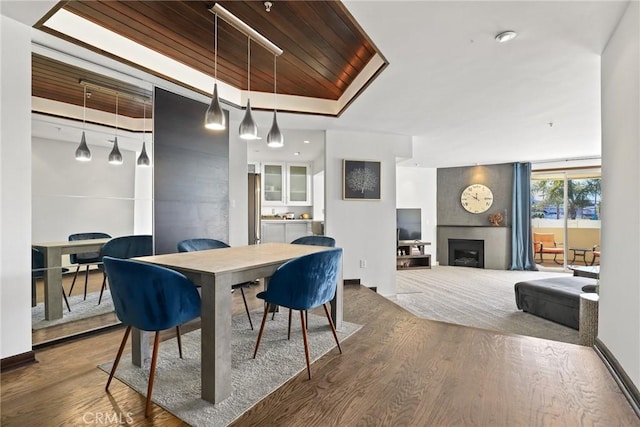 dining area featuring a raised ceiling, wood finished floors, a fireplace, and wooden ceiling