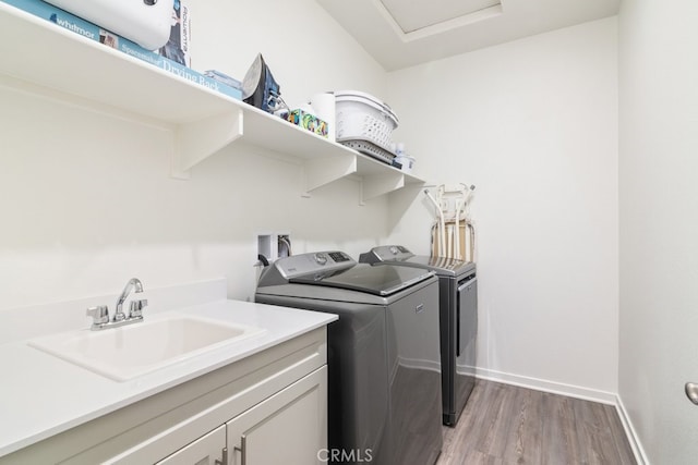 laundry area with light wood-type flooring, a sink, cabinet space, baseboards, and washing machine and clothes dryer