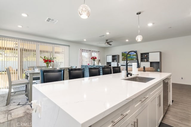 kitchen with visible vents, pendant lighting, an island with sink, a sink, and wood finished floors