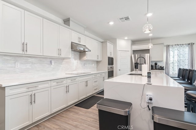 kitchen with visible vents, pendant lighting, under cabinet range hood, a sink, and backsplash