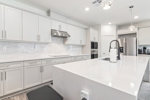 kitchen with visible vents, a sink, under cabinet range hood, black appliances, and a kitchen island with sink