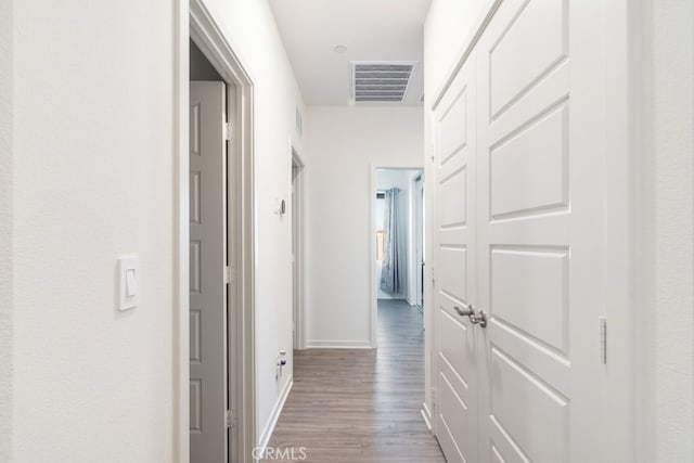 corridor featuring wood finished floors, visible vents, and baseboards