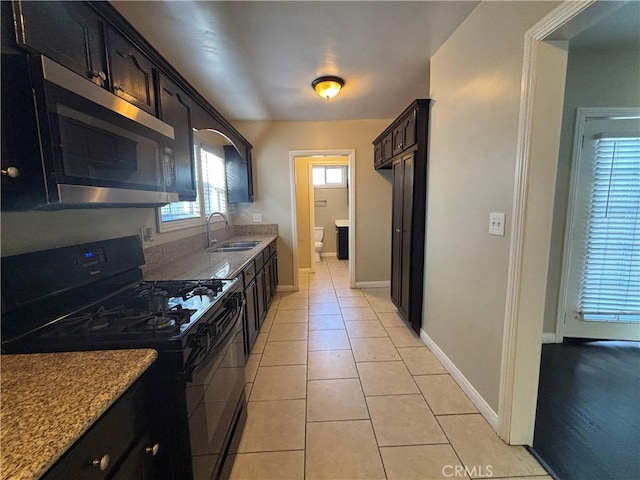 kitchen featuring stainless steel microwave, baseboards, light tile patterned floors, black range with gas cooktop, and a sink