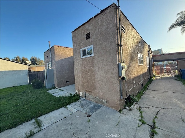 view of property exterior with a gate, fence, a yard, stucco siding, and crawl space