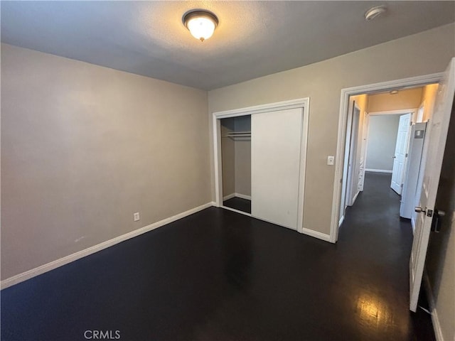 unfurnished bedroom with dark wood-style flooring, baseboards, and a closet