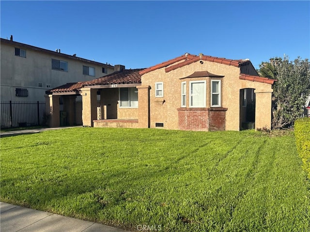 view of front facade with stucco siding, a tile roof, a front yard, and fence