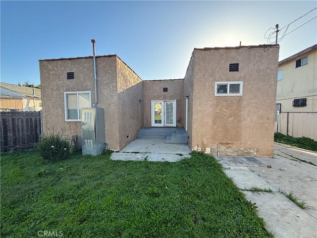 rear view of property with stucco siding, fence, and french doors