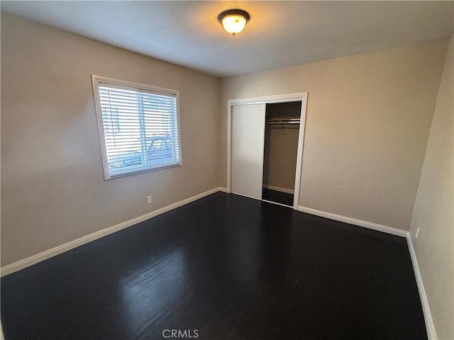 unfurnished bedroom with a closet, baseboards, and dark wood finished floors