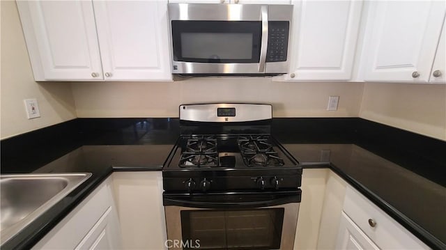 kitchen featuring dark countertops, appliances with stainless steel finishes, white cabinetry, and a sink