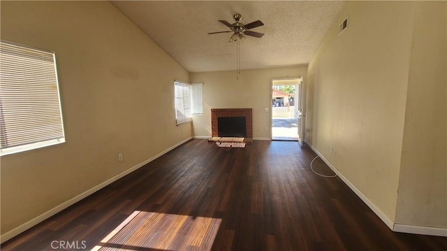 unfurnished living room featuring visible vents, a textured ceiling, wood finished floors, baseboards, and a brick fireplace