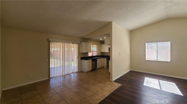 unfurnished living room featuring a sink, a textured ceiling, dark wood-style floors, baseboards, and vaulted ceiling