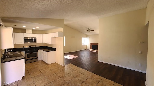 kitchen featuring dark countertops, a fireplace, stainless steel appliances, a ceiling fan, and a sink