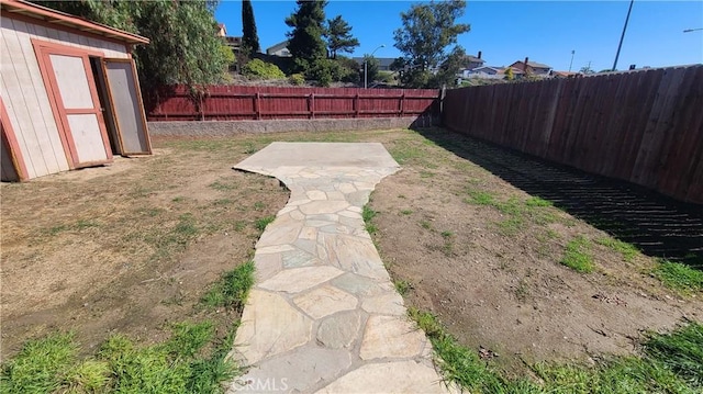 view of yard with an outdoor structure, a storage unit, a fenced backyard, and a patio