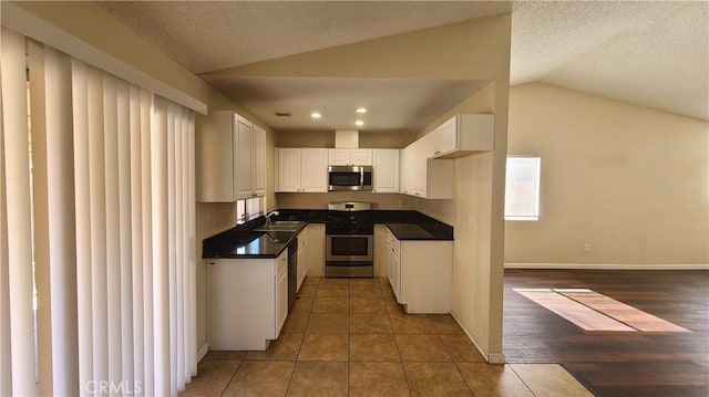 kitchen with lofted ceiling, tile patterned flooring, white cabinets, appliances with stainless steel finishes, and dark countertops